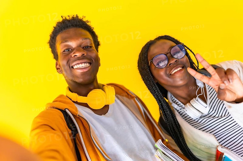 Studio portrait with yellow background of African students taking selfie and gesturing success with fingers smiling at camera