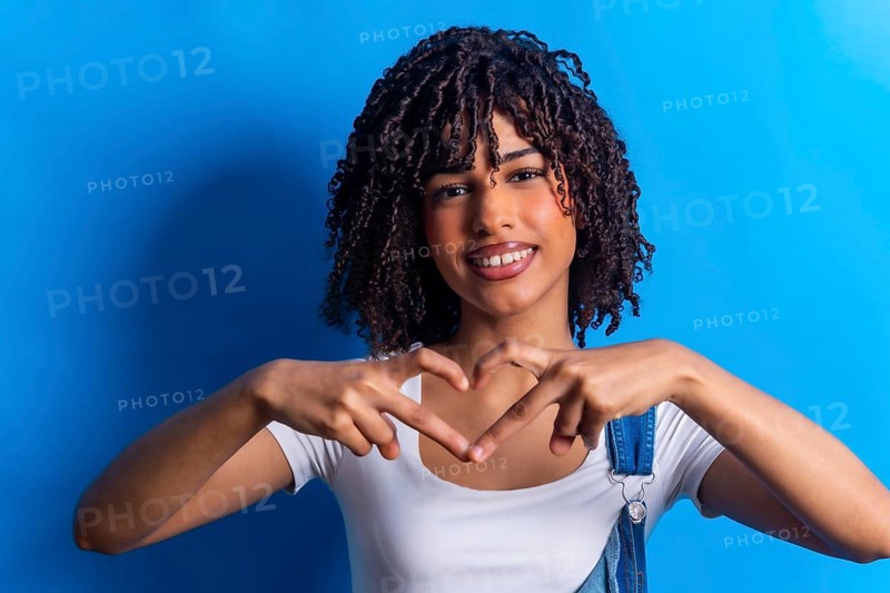 Smiling young woman making heart shape with hands, expressing love and affection on vibrant blue background