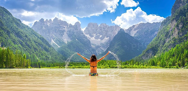 Young woman enjoying summer vacations, splashing water in the scenic lago di landro, surrounded by the breathtaking dolomites mountain range in italy