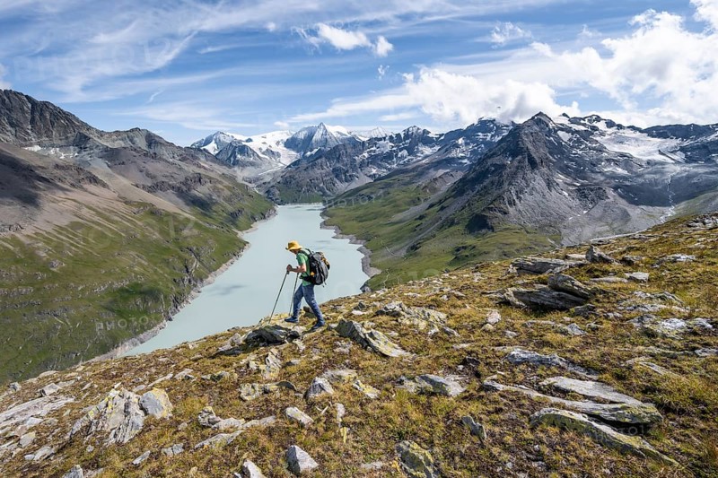 Mountaineer on the summit of Mont de la Blana, view of a blue mountain lake, Lac des Dix reservoir, behind mountain peak Mont Blanc de Cheilon with glacier, Hérménence, Valais Alps, Valais, Switzerland, Europe
