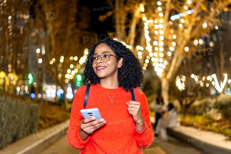 Smiling student walking in a decorated city using her smartphone during christmas holidays