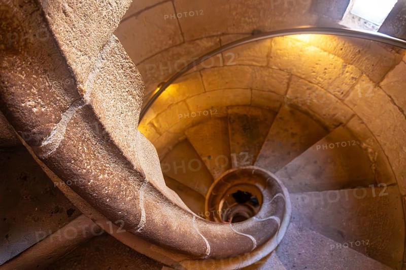 Warm light illuminating ancient stone spiral staircase descending into the depths of barcelona cathedral, a captivating architectural marvel