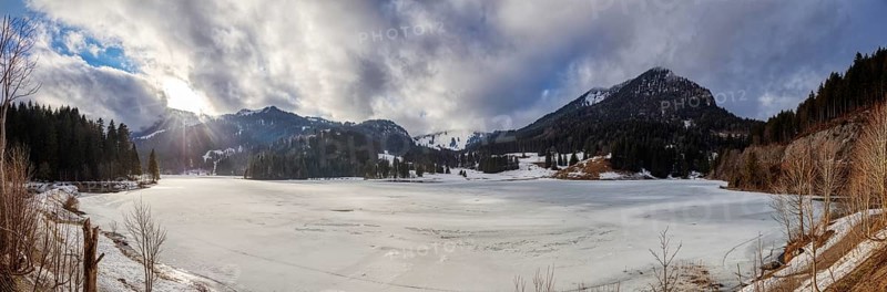 Snowy winter landscape with mountains, densely wooded slopes and partly cloudy skies, Spitzingsee