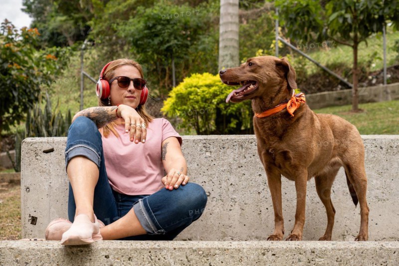 A tranquil woman with headphones sits in the plaza accompanied by her faithful pet