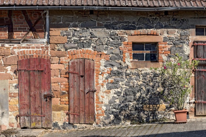 Historic farmhouse around 1800, half-timbered façade, sandstone, natural stone, brick, weathered wooden doors to stable and loo, flower pot with rhododendron, idyllic, romantic, Nidda, Vogelsberg, Wetterau, Hesse, Germany, Europe