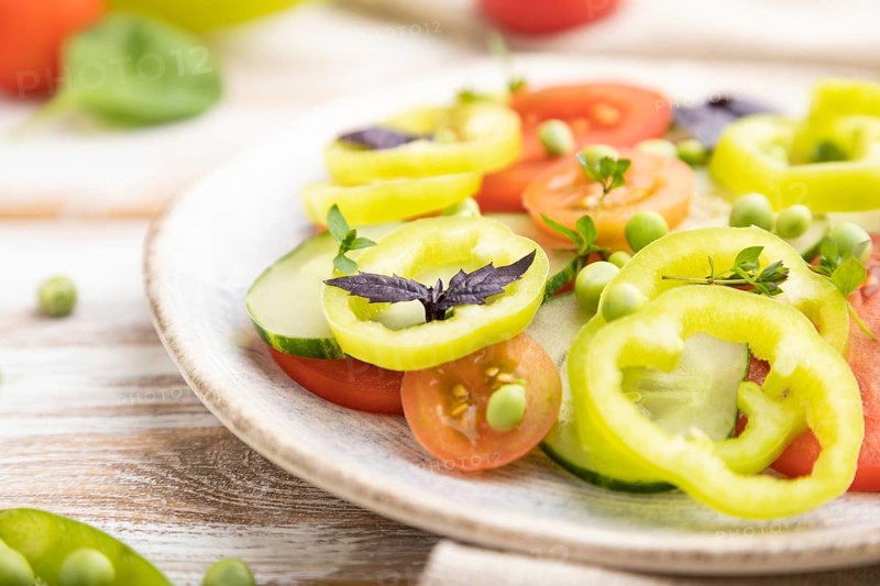 Vegetarian salad from green pea, tomatoes, pepper and basil on white wooden background and linen textile. Side view, close up, selective focus