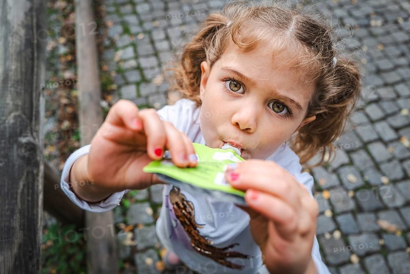 A young girl with pigtails eats a snack on a cobbled street and looks curiously, Stuttgart, Baden-Württmeberg, Germany, Europe