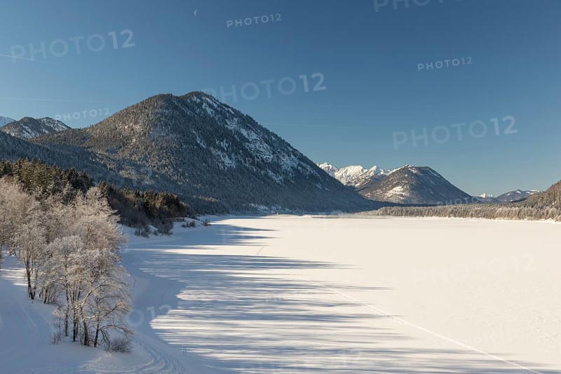 Frozen Sylvenstein reservoir, covered with snow. Isar valley in winter at temperatures of minus 18 degrees Celsius. Snow covered landscape with the Isar river flowing through. Some hoar frosted trees. Early morning at sunrise
