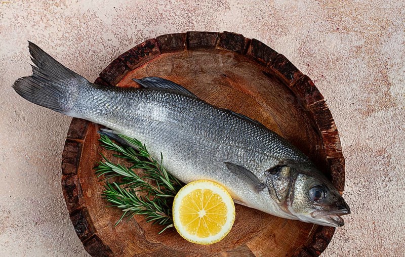 Fresh, raw sea bass fish, in a wooden plate, top view, no people