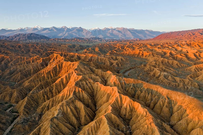 River bed runs through a landscape of eroded hills, badlands at sunset, mountain peaks of the Tian Shan Mountains in the background, aerial view, Canyon of the Forgotten Rivers, Issyk Kul, Kyrgyzstan, Asia