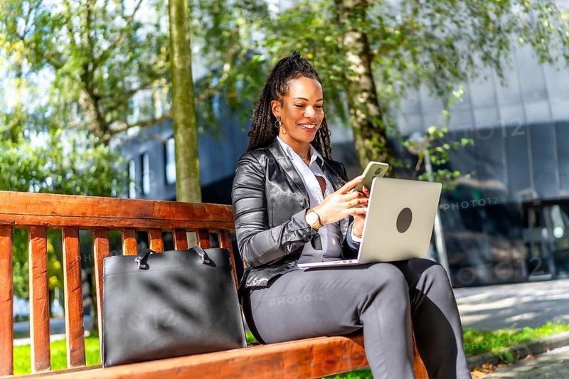 Latin elegant businesswoman using mobile phone while working with laptop on remote sitting outdoors