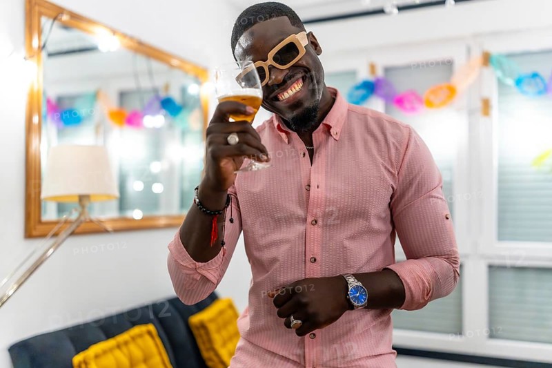 African man wearing sunglasses smiling and toasting at camera during a home party