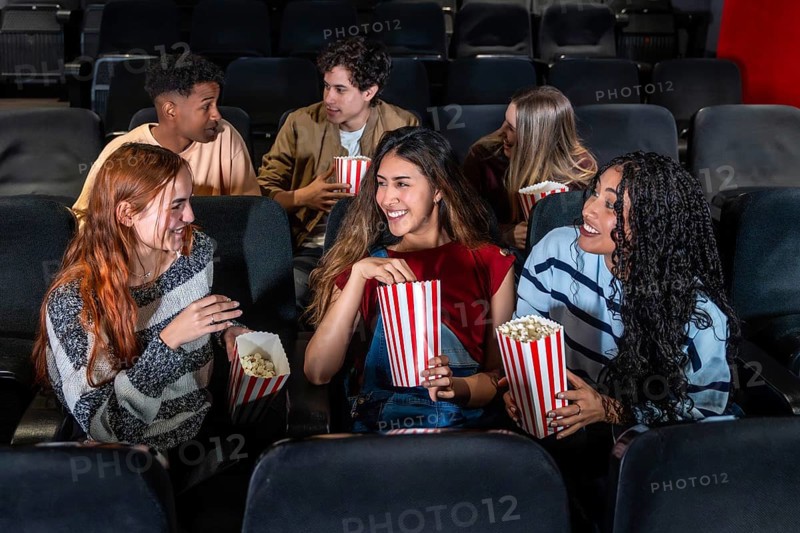 Cheerful multi ethnic friends enjoying popcorn while watching a film together in a cozy movie theater, sharing laughs and smiles