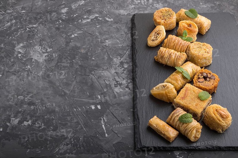 Traditional arabic sweets (kunafa, baklava) on a black slate board on a black concrete background. side view, copy space