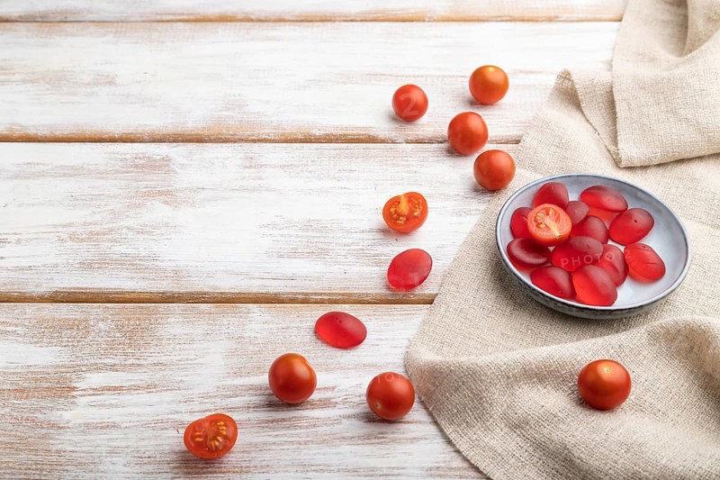 Jelly tomato candies on white wooden background and linen textile. copy space, side view