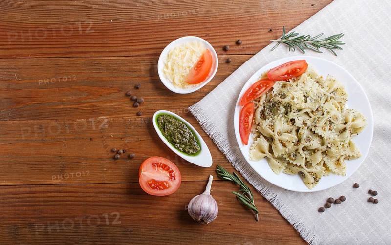 Farfalle pasta with pesto sauce, tomatoes and cheese on a linen tablecloth on brown wooden background. top view, copy space