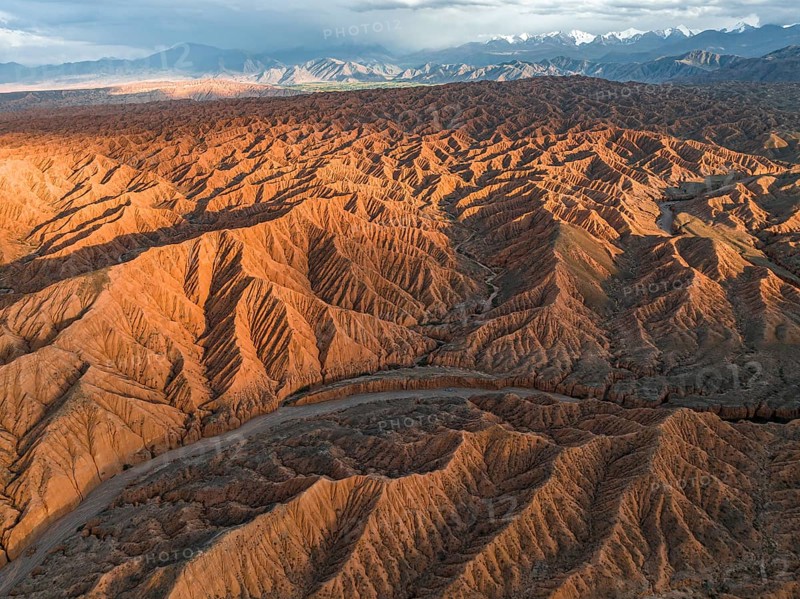 River bed runs through a landscape of eroded hills, badlands at sunset, mountain peaks of the Tian Shan Mountains in the background, aerial view, Canyon of the Forgotten Rivers, Issyk Kul, Kyrgyzstan, Asia