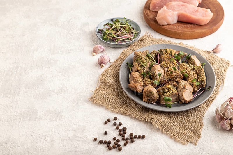 Stewed turkey fillet with garlic and sprouts of radish on white wooden background and linen textile. Side view, copy space