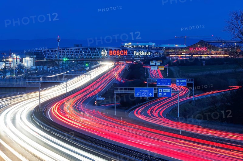 A8 motorway at Stuttgart Airport in the evening. Heavy traffic, lanes of light. Modern architecture of Messe Stuttgart with multi-storey car park above the motorway lanes. Logo of the Bosch company. Stuttgart, Baden-Württemberg, Germany, Europe