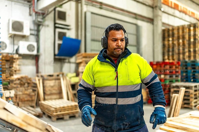 Man caucasian worker with dirty reflective clothes working in a recycling plant arranging pallets for reuse