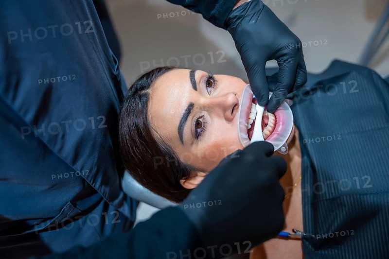 Dentist wearing black gloves applying teeth whitening gel to a female patient in a dental clinic