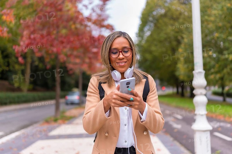 Frontal portrait of a happy distracted latin woman using phone walking along the street