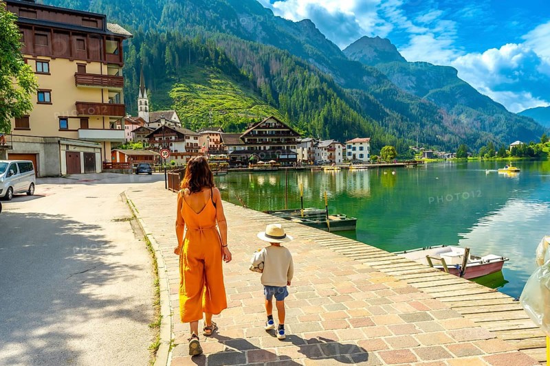 Mother and son walking on a paved pathway by the alleghe lake in the italian dolomites, enjoying summer holidays