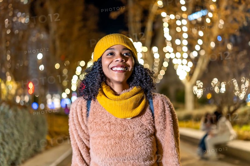 Portrait of a young woman wearing winter clothes, enjoying christmas lights in a decorated city at night