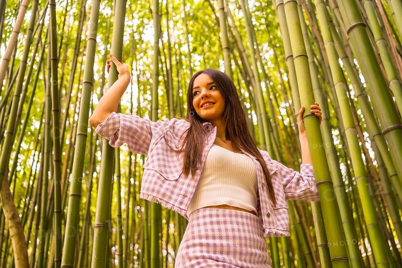 Young caucasian girl with a pink skirt in a bamboo forest. Enjoying summer holidays in a tropical climate, walking in the forest grabbing the trunks of bamboo and smiling