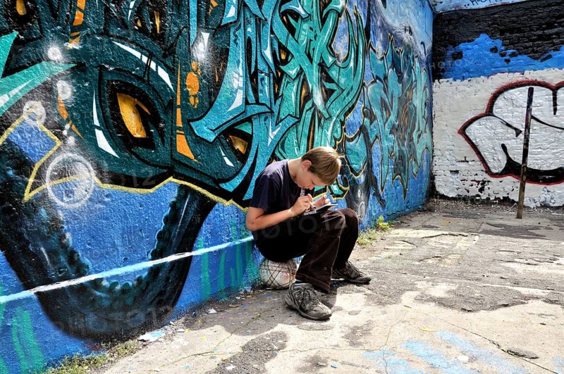 Ten-year-old boy playing with his Nintendo in front of a graffiti wall, football pitch, Germany, Europe