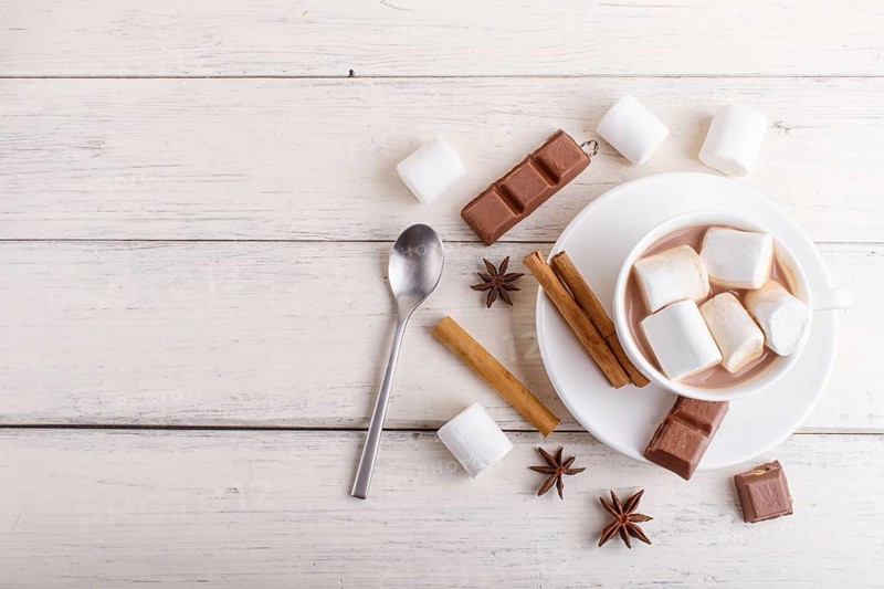 A cup of hot chocolate with marshmallow and spices on white wooden background. top view, copy space