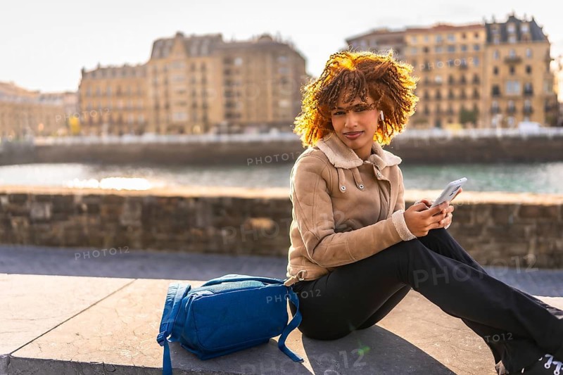 Side view with copy space of a latin beauty woman using phone sitting next to the river at city