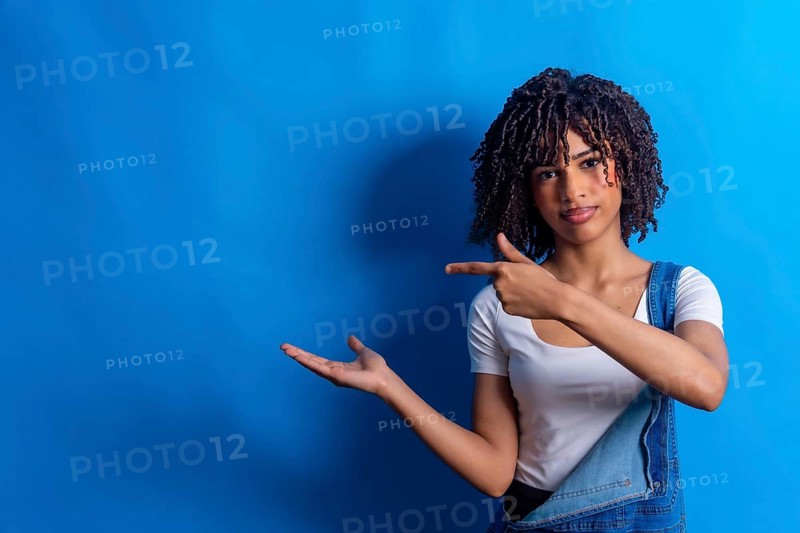 Young woman pointing her finger to the side and showing something with her open hand on a vibrant blue background