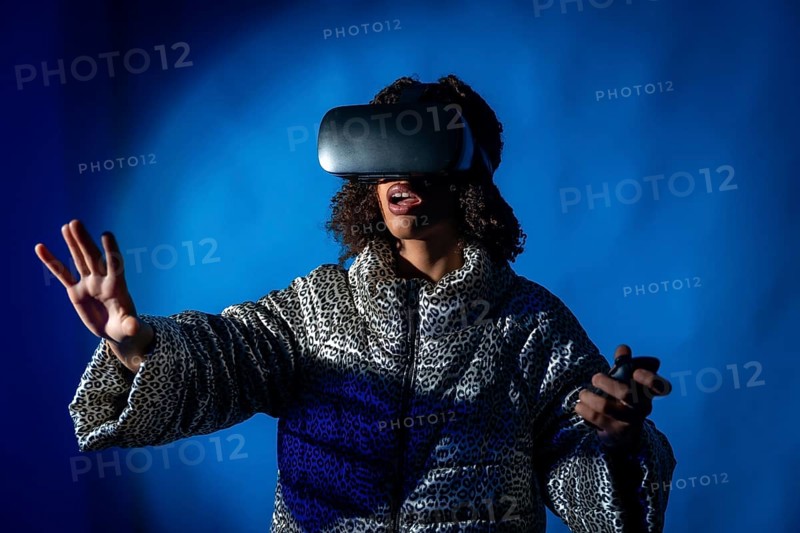 Young woman wearing a vr headset and holding controllers, expressing surprise while immersing in virtual reality against a blue background