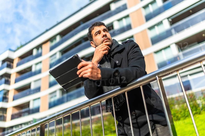 Low angle view potrait of a caucasian pensive businessman in casual winter clothes using digital tablet standing in the city
