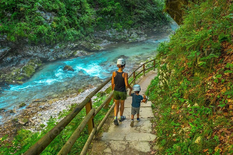 Tourists wearing helmets are enjoying a summer walk along the stunning turquoise radovna river flowing through the vintgar gorge near bled, slovenia