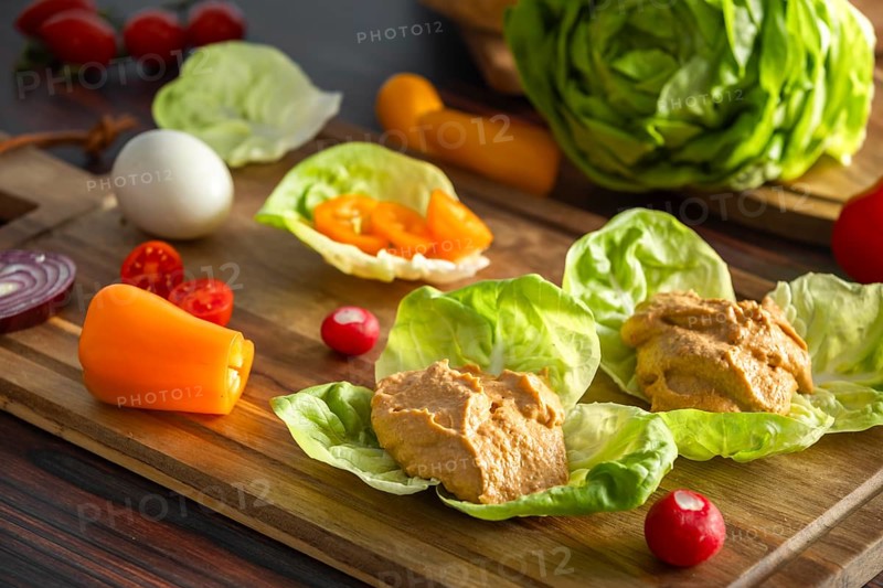 Leaf salad with hummus and fresh vegetables, including peppers and radishes, on a board