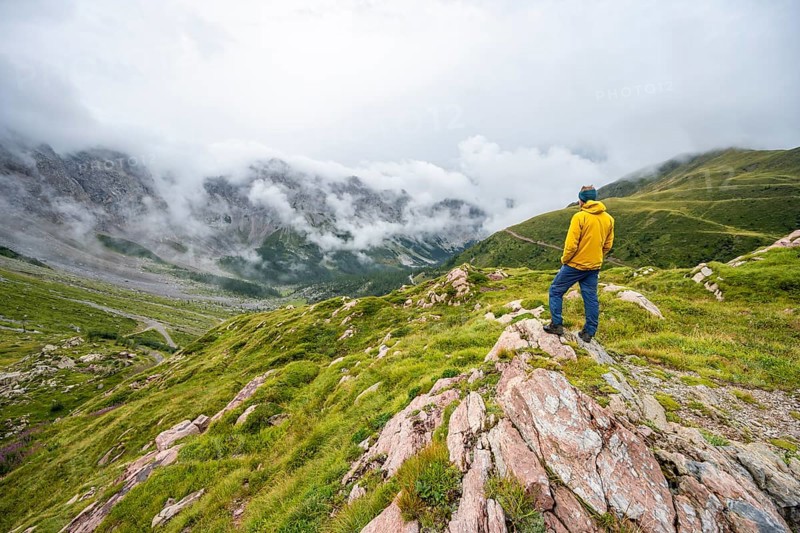 Mountaineer with yellow jacket looking at mountain landscape, cloudy rocky mountain peaks Wolayer Köpf and Biegenköpfe, Carnic Alps, Carnic High Trail, Carinthia, Austria, Europe