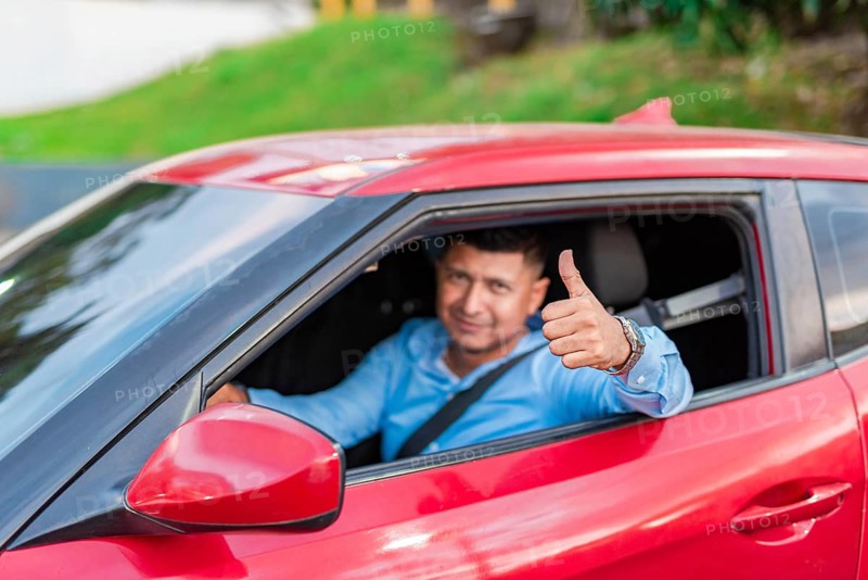 Smiling driver in his car giving a thumbs up. Male driver showing thumbs up while driving