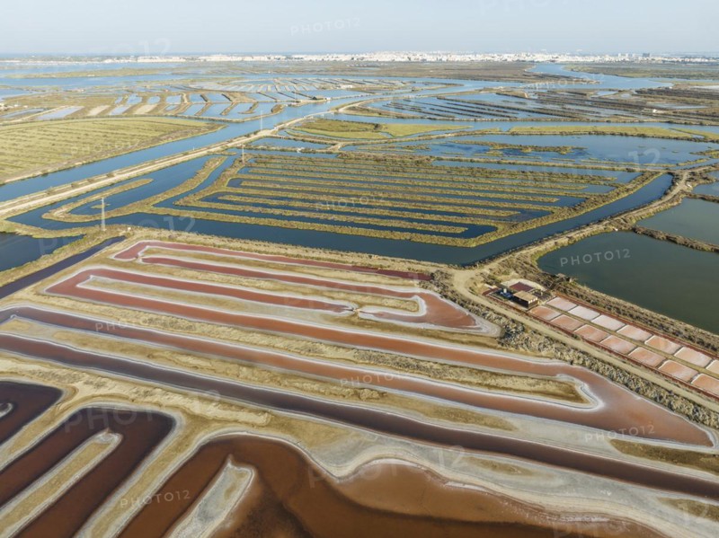 Saline ponds at the salt works near Chiclana de la Frontera. The orange-red colour depends on the level of salinity and is directly caused by the algae Dunaliella salina and brine shrimp. Aerial view. Drone shot. Bahía de Cádiz Nature Reserve, Cádiz province, Andalusia, Spain, Europe