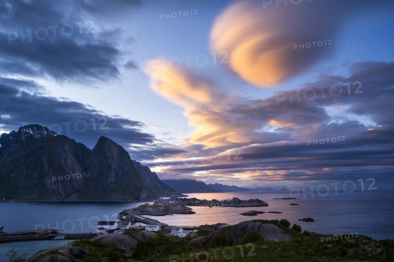 Cloudy landscape. The villages of Olenilsoy, Toppoya (Toppoy) and Hamnoy as well as the Festhaeltinden mountain. A bridge connects the islands. View across the sea towards Flakstadoya and Vestvagoya. Several coloured lenticular clouds (lenticularis) in the blue sky. At night at the time of the midnight sun. Early summer. Moskenesoya, Lofoten, Norway, Europe