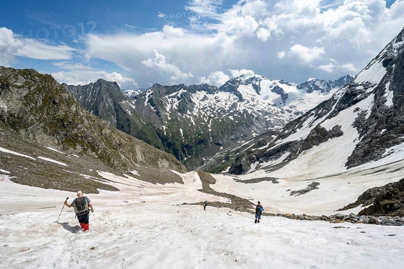 Mountaineers hiking in a snowfield, Nördliche Mörchnerscharte, behind mountain peak Kleiner Mörchner and Greizer Spitze with snow, Berliner Höhenweg, Zillertal Alps, Tyrol, Austria, Europe
