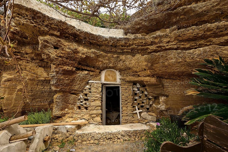 Exterior view of a cave carved into the rock with a stone wall and vegetation around the entrance, Agios Nikolaos rock church, Oasis Beach, Kallithea, Rhodes, Dodecanese, Greek Islands, Greece, Europe