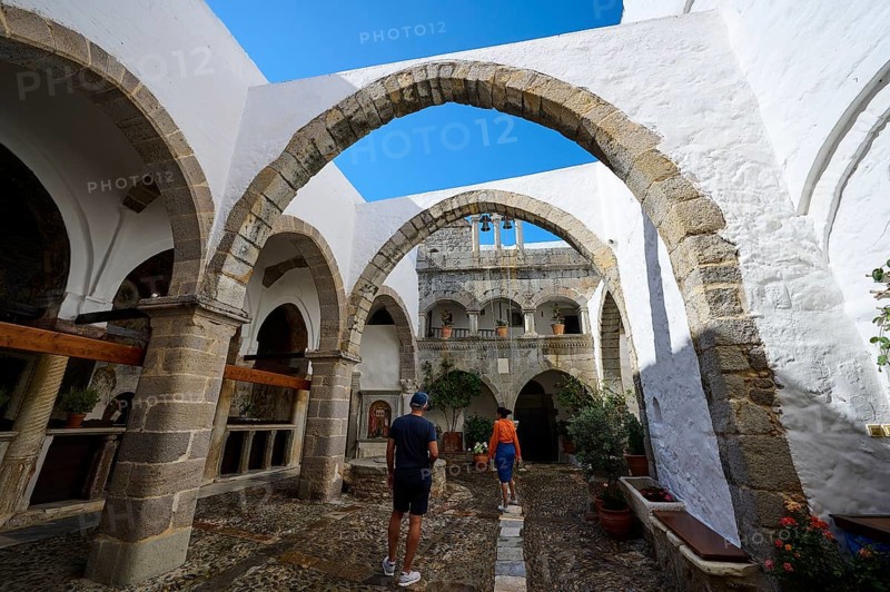 Historic monastery courtyard with stone arcades and bright white walls. Tourists explore the architectural beauty, Inside the monastery, Agiou Theologou Monastery, Chora, Patmos, Dodecanese, Greek Islands, Greece, Europe