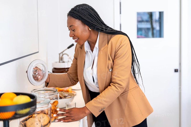 Businesswoman taking cookies from glass jar at hotel buffet, enjoying breakfast during her business trip