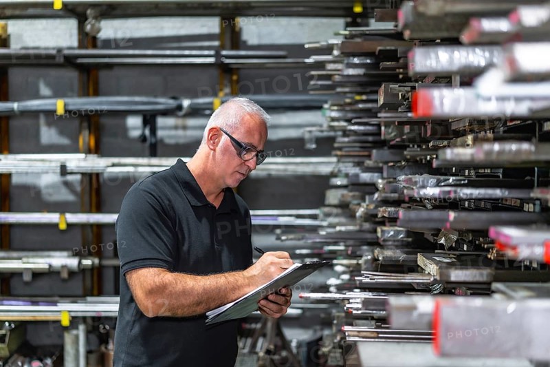 Side view photo of a mature caucasian man checking metal bars while doing inventory using a clipboard in a factory