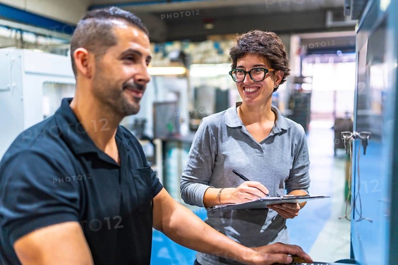 Male manual worker talking with female manager while using computer in the factory