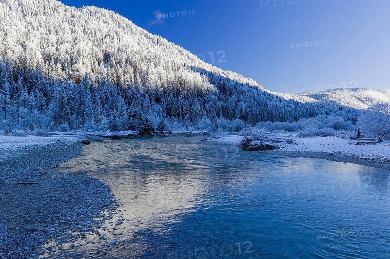 Isar valley in winter at temperatures of minus 18 degrees Celsius. Snow covered landscape with the Isar river flowing through. Some hoar frosted trees. Early morning