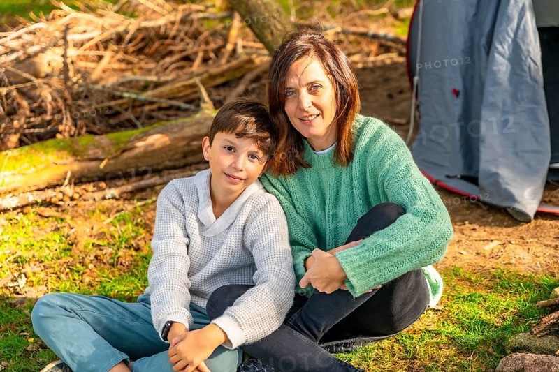 Caucasian mother and son smiling at camera sunbathing enjoying nature in the forest next to camping tent