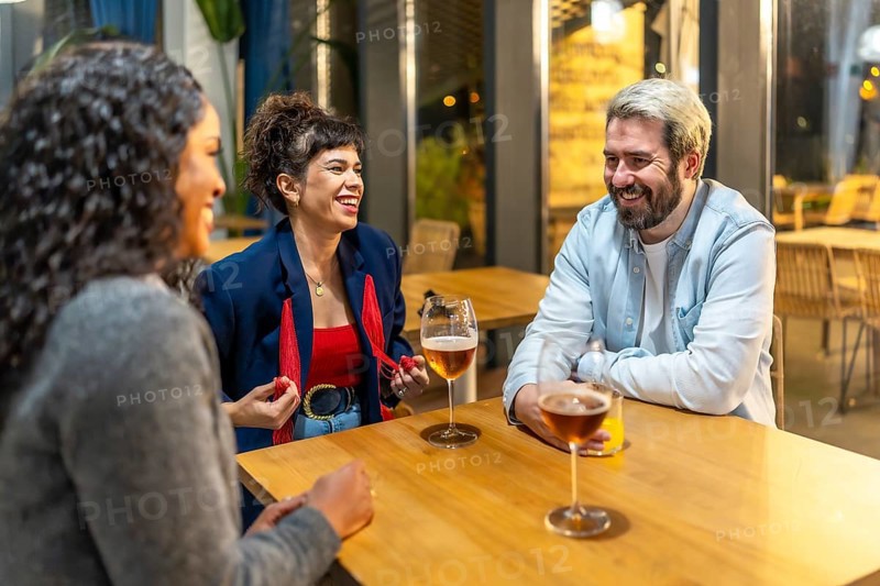 Multiracial friends enjoying night talking and drinking beer and cocktail in a bar terrace